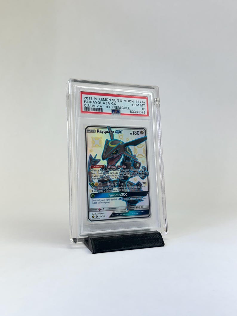 May include: A graded Pok&eacute;mon card featuring Rayquaza GX, encased in a clear protective holder. The card is displayed on a black stand. The label reads "2018 POKEMON SUN & MOON #177b FA/RAYQUAZA GX". The card is graded GEM MT 10.