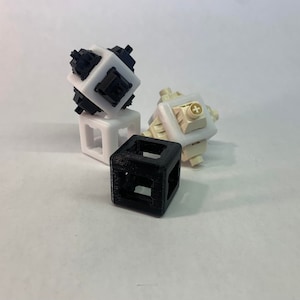 Peut inclure: Trois cubes imprimés en 3D, un noir, un blanc et un beige. Le cube noir est en bas, le cube blanc est au-dessus du cube noir et le cube beige est au-dessus du cube blanc.