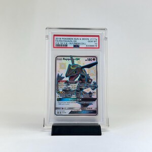May include: A graded Rayquaza GX Pok&eacute;mon card from the 2018 Sun & Moon set. The card is encased in a clear protective holder and displayed on a black stand. The card features a green and blue Rayquaza illustration.