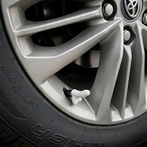 May include: Close-up of a silver alloy wheel with a black tire. The tire has the word "BFGoodrich" printed on it. A white, novelty valve stem cap shaped like a hand is visible.