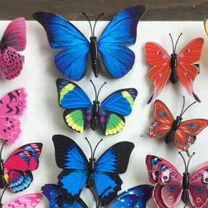 May include: Assortment of colorful butterfly hair clips. The clips feature various designs and colors, including blue, red, pink, and green. The butterflies are made of plastic and have a shiny finish.