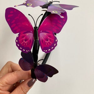 May include: A black headband with three purple butterflies attached. The butterflies have iridescent wings with a dark purple and light purple color gradient.