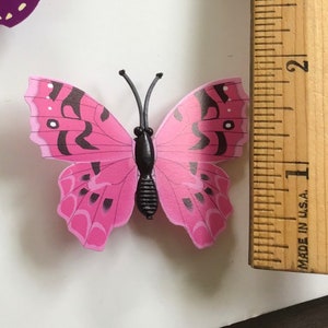 May include: Pink butterfly with black markings and a black body. The butterfly is about 1 inch wide.