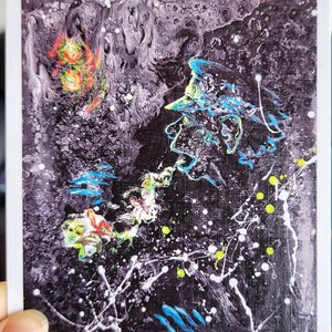 May include: Abstract painting with a black background and splashes of white, blue, green, and yellow paint. The painting features a figure with a hat and a blue and green color scheme. The painting is signed "@martisha_in_the_sea".