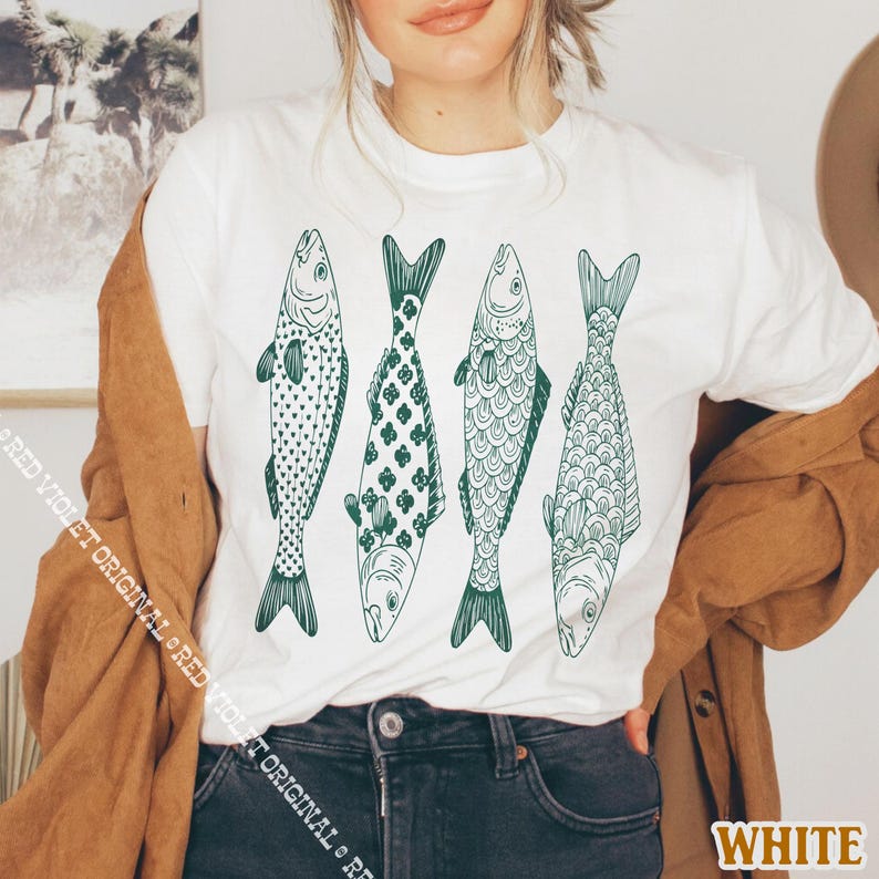 Op de afbeelding: Wit t-shirt met vier groene visillustraties. De vissen hebben verschillende patronen, waaronder harten, bloemmotieven en schubachtige details. Het woord "WHITE" is rechtsonder zichtbaar.