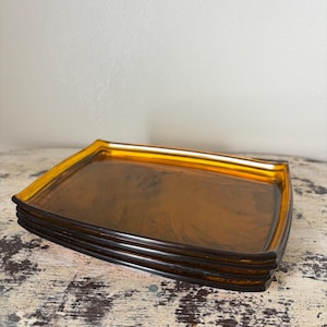 May include: A stack of four amber-colored rectangular trays. The trays have a glossy finish and a slightly raised edge. The trays are stacked on top of each other, creating a layered effect. The trays are made of a translucent material.