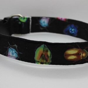 Puede incluir: Collar de perro negro con estampado de escarabajos coloridos. El collar est&aacute; hecho de tela y tiene una hebilla de pl&aacute;stico.