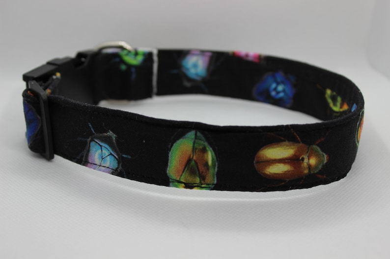 Puede incluir: Collar de perro negro con estampado de escarabajos coloridos. El collar est&aacute; hecho de tela y tiene una hebilla de pl&aacute;stico.