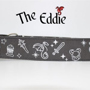 May include: A grey dog collar featuring white illustrations of a dragon, sword, potion bottle, and other fantasy-themed symbols. The collar has the text "The Eddie" printed on it.