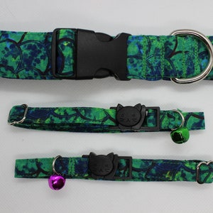 May include: Three cat collars in a green and blue floral pattern. The largest collar has a black buckle and a silver D-ring. The two smaller collars have a black cat-shaped buckle and a silver bell.
