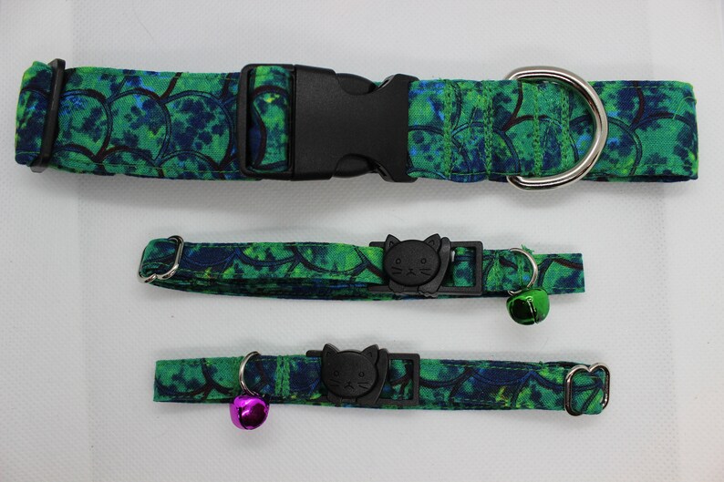 May include: Three cat collars in a green and blue floral pattern. The largest collar has a black buckle and a silver D-ring. The two smaller collars have a black cat-shaped buckle and a silver bell.