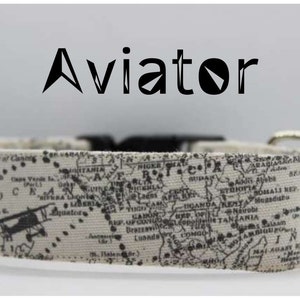 May include: A white dog collar with a black and white world map print and a small airplane graphic. The collar has a black buckle and a silver ring. The word "Aviator" is printed in black above the collar.