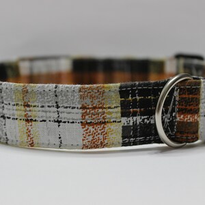 Op de afbeelding: Een bruin, zwart en wit geruit hondenhalsband met een zwarte gesp en een zilveren D-ring.