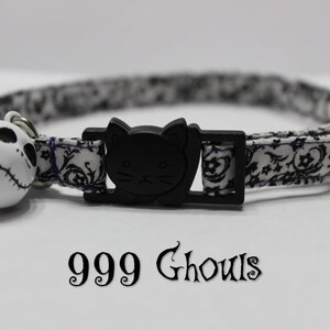 May include: Black and white patterned cat collar with a black cat head buckle and a white bell with a black and white Jack Skellington face. The collar has the text "999 Ghouls" printed on it.
