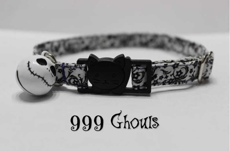 May include: Black and white patterned cat collar with a black cat head buckle and a white bell with a black and white Jack Skellington face. The collar has the text "999 Ghouls" printed on it.