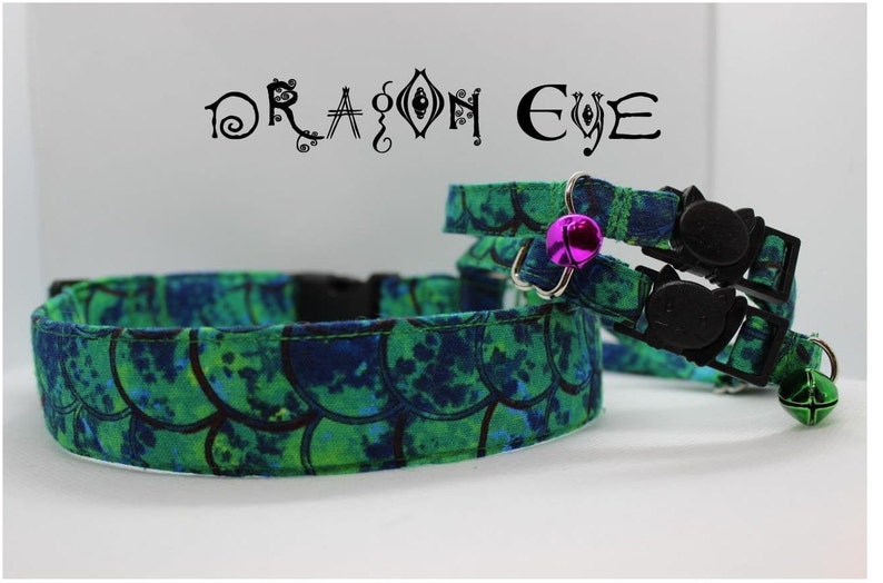 May include: Two green and blue cat collars with a black safety buckle and a bell. The collars have a mermaid scale pattern and the text "DRAGON EYE" is printed above the collars.