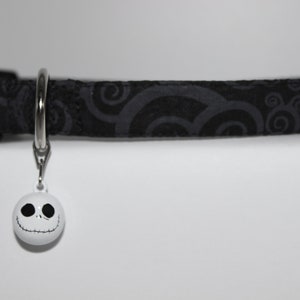 May include: Black cat collar with a white swirl pattern and a white bell with a black Jack Skellington face.