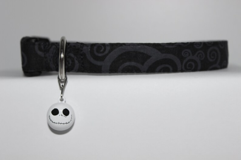 May include: Black cat collar with a white swirl pattern and a white bell with a black Jack Skellington face.
