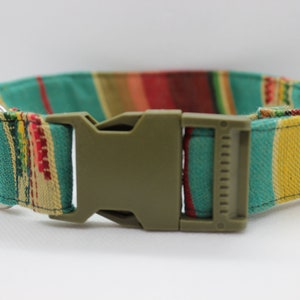 Puede incluir: Un collar de perro a rayas verdes, amarillas, rojas y marrones con un anillo en D plateado y una hebilla de pl&aacute;stico verde.