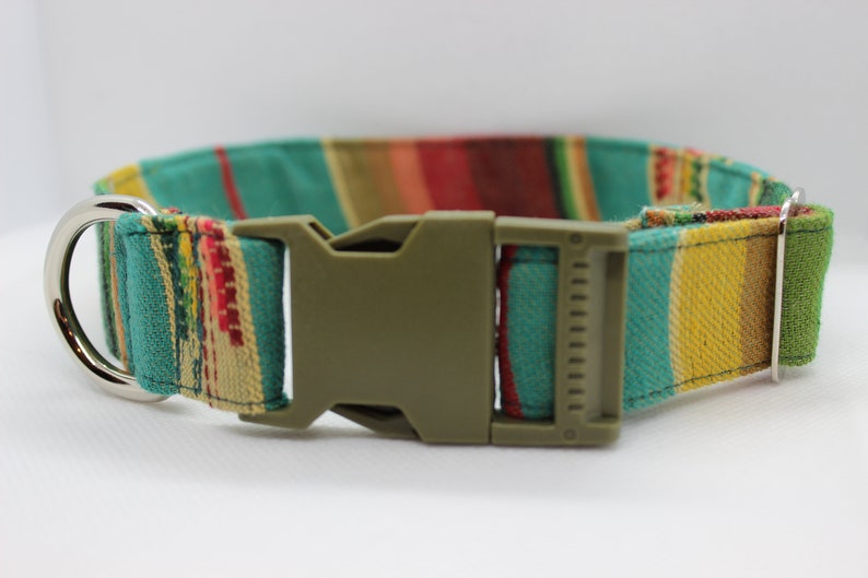 Puede incluir: Un collar de perro a rayas verdes, amarillas, rojas y marrones con un anillo en D plateado y una hebilla de pl&aacute;stico verde.