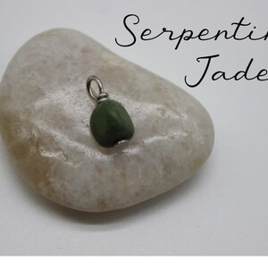 Puede incluir: Un peque&ntilde;o colgante de jade serpentina verde oscuro con una anilla de plata. El colgante est&aacute; sobre una piedra gris clara.