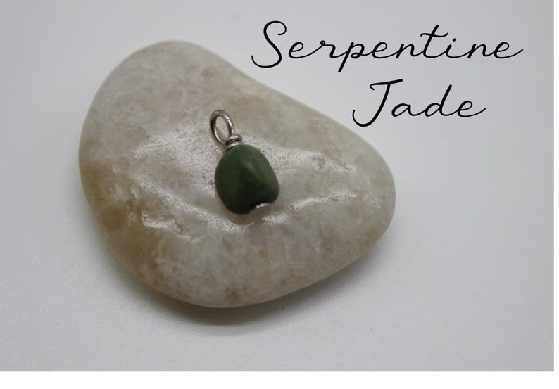 Puede incluir: Un peque&ntilde;o colgante de jade serpentina verde oscuro con una anilla de plata. El colgante est&aacute; sobre una piedra gris clara.