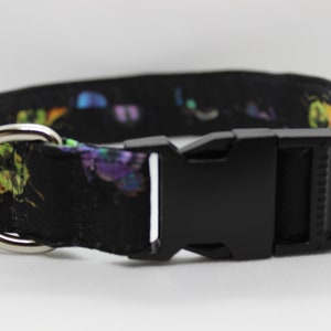 Puede incluir: Un collar de perro negro con estampado de mariposas de colores y una hebilla de pl&aacute;stico negra. El collar tiene un anillo en D de metal plateado.