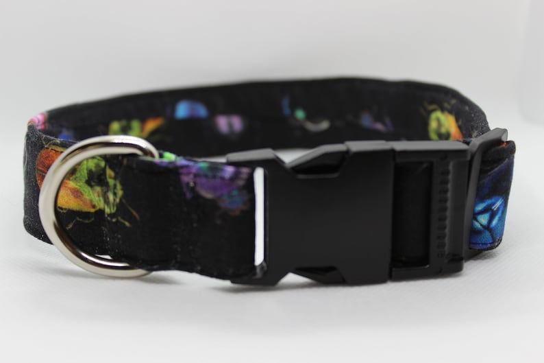 Puede incluir: Un collar de perro negro con estampado de mariposas de colores y una hebilla de pl&aacute;stico negra. El collar tiene un anillo en D de metal plateado.