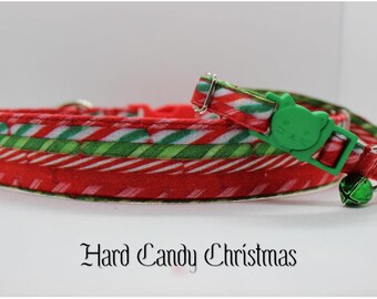 May include: Red and green striped cat collar with a green cat-shaped buckle and a green bell. The collar is made of fabric and has a "Hard Candy Christmas" text label.