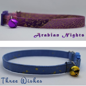 K&ouml;nnte beinhalten: Zwei Katzenhalsb&auml;nder mit Gl&ouml;ckchen. Das erste Halsband ist lila mit einem goldenen Muster und einer lila Glocke. Das zweite Halsband ist blau mit goldenen Punkten und einer goldenen Glocke. Der Text "Arabian Nights" befindet sich unter dem ersten Halsband und "Three Wishes" unter dem zweiten Halsband.