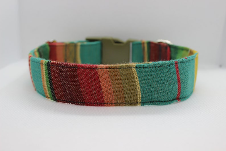 Puede incluir: Un collar de perro a rayas de colores con un patr&oacute;n verde, rojo, amarillo y marr&oacute;n. El collar tiene un cierre de hebilla.