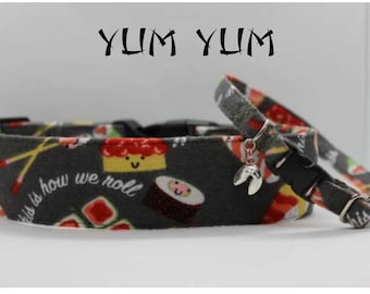 May include: A gray and red cat collar with a sushi print and the text "This is how we roll". The collar has a silver charm shaped like a sushi roll.
