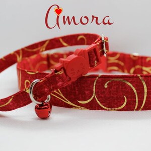 May include: Red cat collar with a gold swirl pattern and a red cat-shaped breakaway buckle. The collar has a small bell attached.