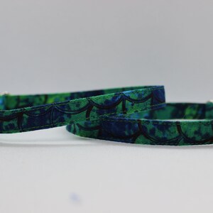 May include: Two green and blue patterned cat collars with a bell on each end. One bell is green and the other is pink.
