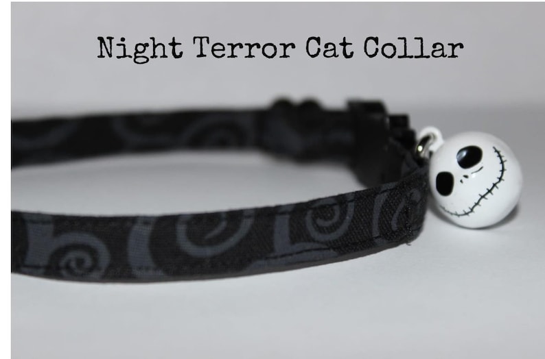 May include: Black cat collar with a gray swirl pattern and a white Jack Skellington bell charm.  "Night Terror Cat Collar" is written above the collar.