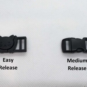 Op de afbeelding: Twee zwarte plastic gespen, een met een kattenontwerp en de tekst "Easy Release" en de andere met de tekst "Medium Release".