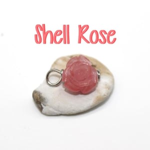 May include: A pink shell rose charm with a silver loop. The charm is sitting on a white seashell.
