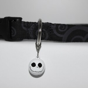 May include: Black and gray patterned dog collar with a silver D-ring and a white bell with a black Jack Skellington face.