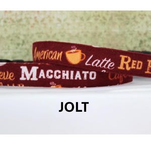 May include: A maroon dog collar with coffee-themed text including "American," "Latte," "Red Eye," "Breve," and "Macchiato." The collar features a metal buckle and the word "JOLT" at the bottom.