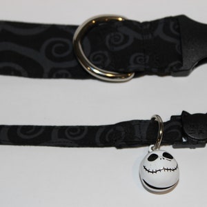 May include: Black cat collar with a black and gray swirl pattern and a silver buckle. The collar has a black cat charm and a white bell with a Jack Skellington face.