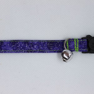 May include: A purple and green cat collar with a silver bell and a black cat-shaped safety buckle.