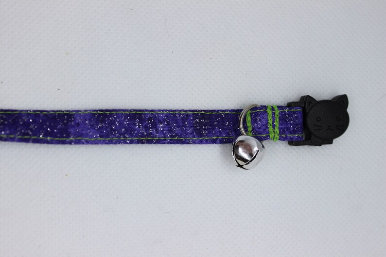 May include: A purple and green cat collar with a silver bell and a black cat-shaped safety buckle.