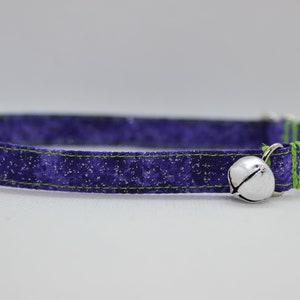 May include: Purple cat collar with a green trim and a silver bell. The collar has a black plastic buckle.