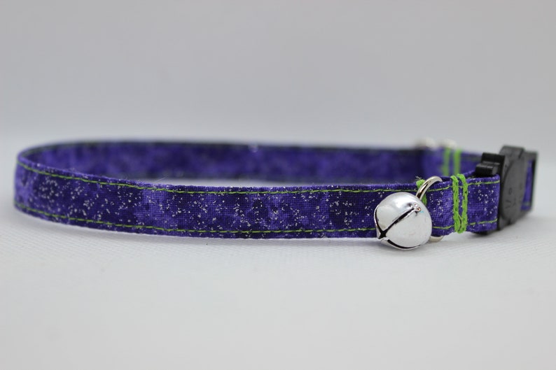 May include: Purple cat collar with a green trim and a silver bell. The collar has a black plastic buckle.