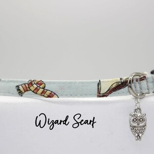 May include: A light blue cat collar with a silver owl charm. The collar has a pattern of wizarding scarves and books. The text "Wizard Scarf" is printed below the collar.