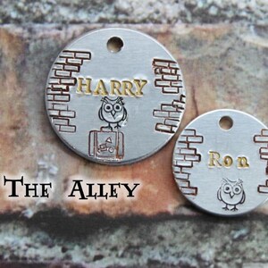 May include: Two silver round metal tags with a brick pattern and an owl design. The first tag says "HARRY" and the second tag says "Ron".