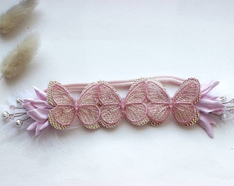 Può includere: Un cerchietto rosa con tre decorazioni a forma di farfalla e un fiore rosa con accenti di perle bianche.
