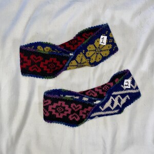 May include: Two knitted headbands with colorful floral and geometric patterns. One headband features a red and black floral design, while the other has a pink and black floral pattern. Both have a blue background and are labeled with numbers.