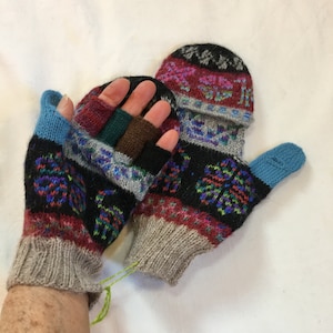 Puede incluir: Un par de mitones de punto con un diseño convertible, con una base negra con coloridos estampados florales en azul, rojo y verde. Los puños y el pulgar son de color gris claro y azul. El mitón de la izquierda tiene aberturas sin dedos.