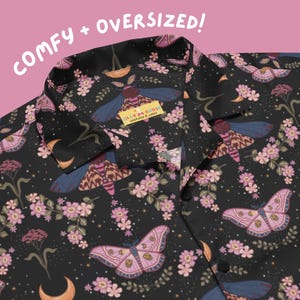 May include: Black button-up shirt with a repeating pattern of pink moths, flowers, and crescent moons. The shirt has a collar and the text "COMFY + OVERSIZED!" is visible. The tag reads "SILLY GOOSE WORKSHOP & GOODS".